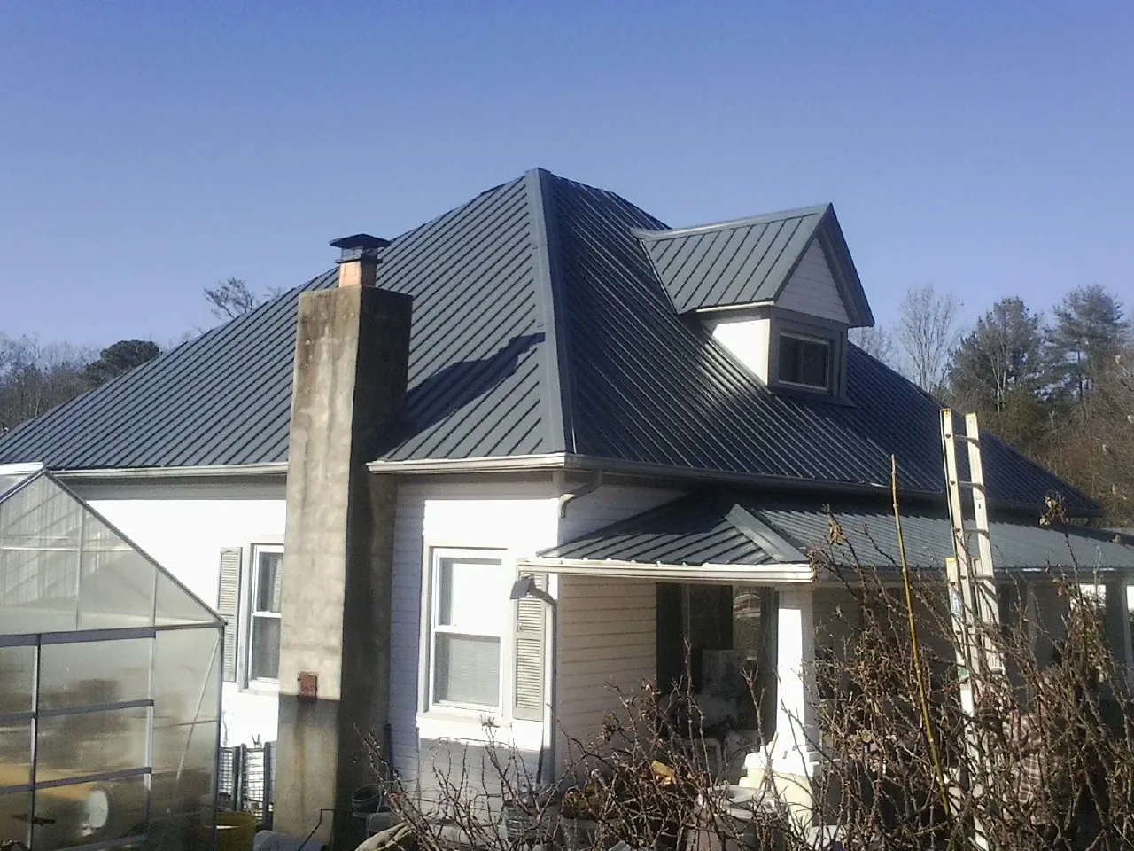 Dark blue standing seam metal roof on a white farmhouse with dormer — Slate & Tile Roof Repair by Roofing Brothers in Glen Flora