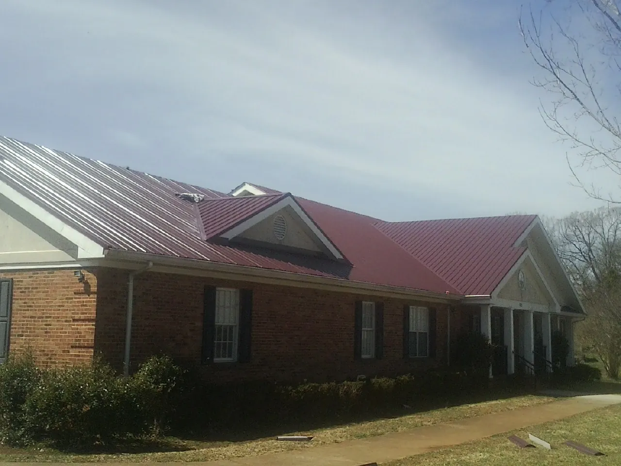 Red metal roof with gabled entries on a long brick building, from a Hail Damage Roof Repair job in Glen Flora