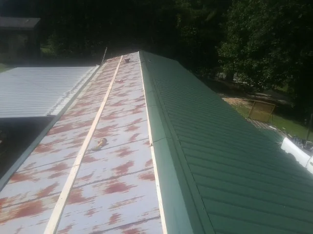 Old rusted panels beside newly installed green metal roofing — Wind Damage Roof Repair by Roofing Brothers in Glen Flora