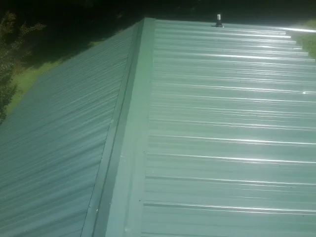 New green metal panels meeting at the ridge of a roof — Flat Roof Repair work by our crew in Glen Flora