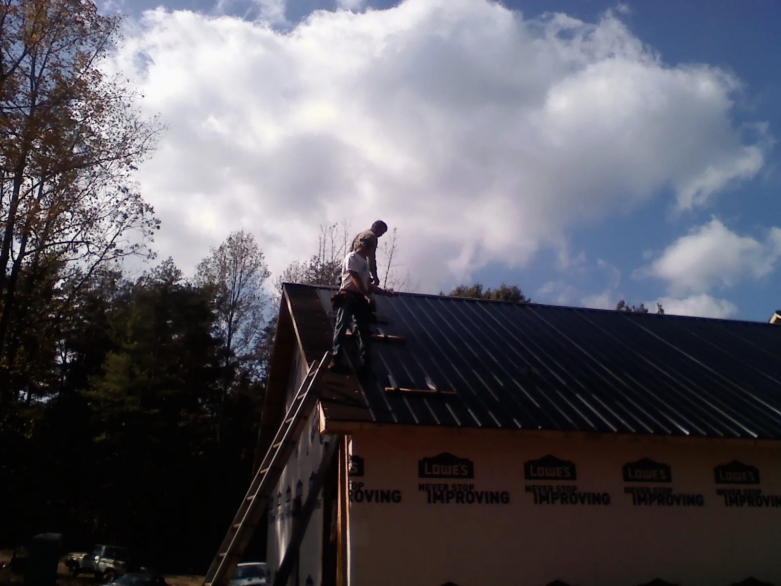 Roofer fastening dark metal panels high against a cloudy sky, from a Roof Inspection job in Glen Flora