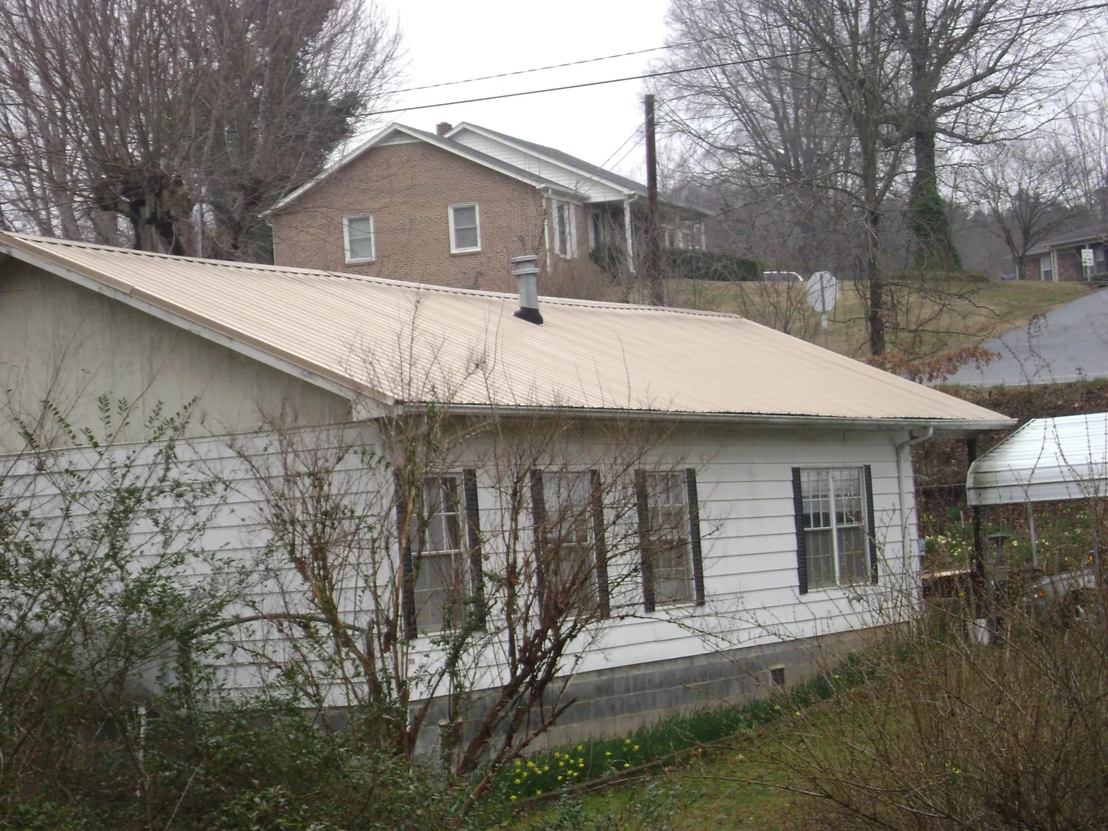 Tan metal roof on a white sided house set into a hillside — Commercial Roofing by Roofing Brothers in Glen Flora