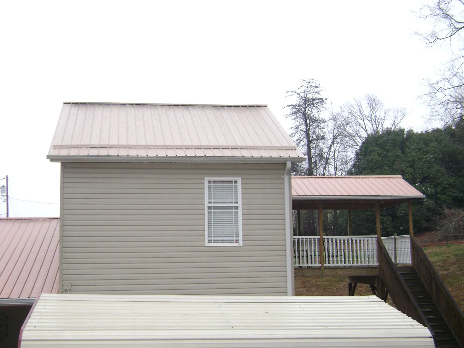 Tan metal roofs on a two story addition and attached porch, from a Roof Replacement job in Glen Flora